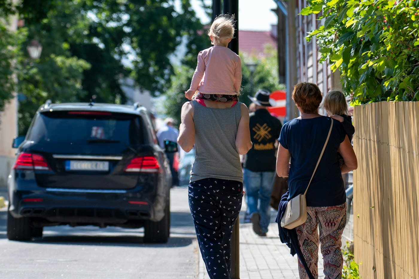 Family walking down a sunny street with a toddler on a parent's shoulders