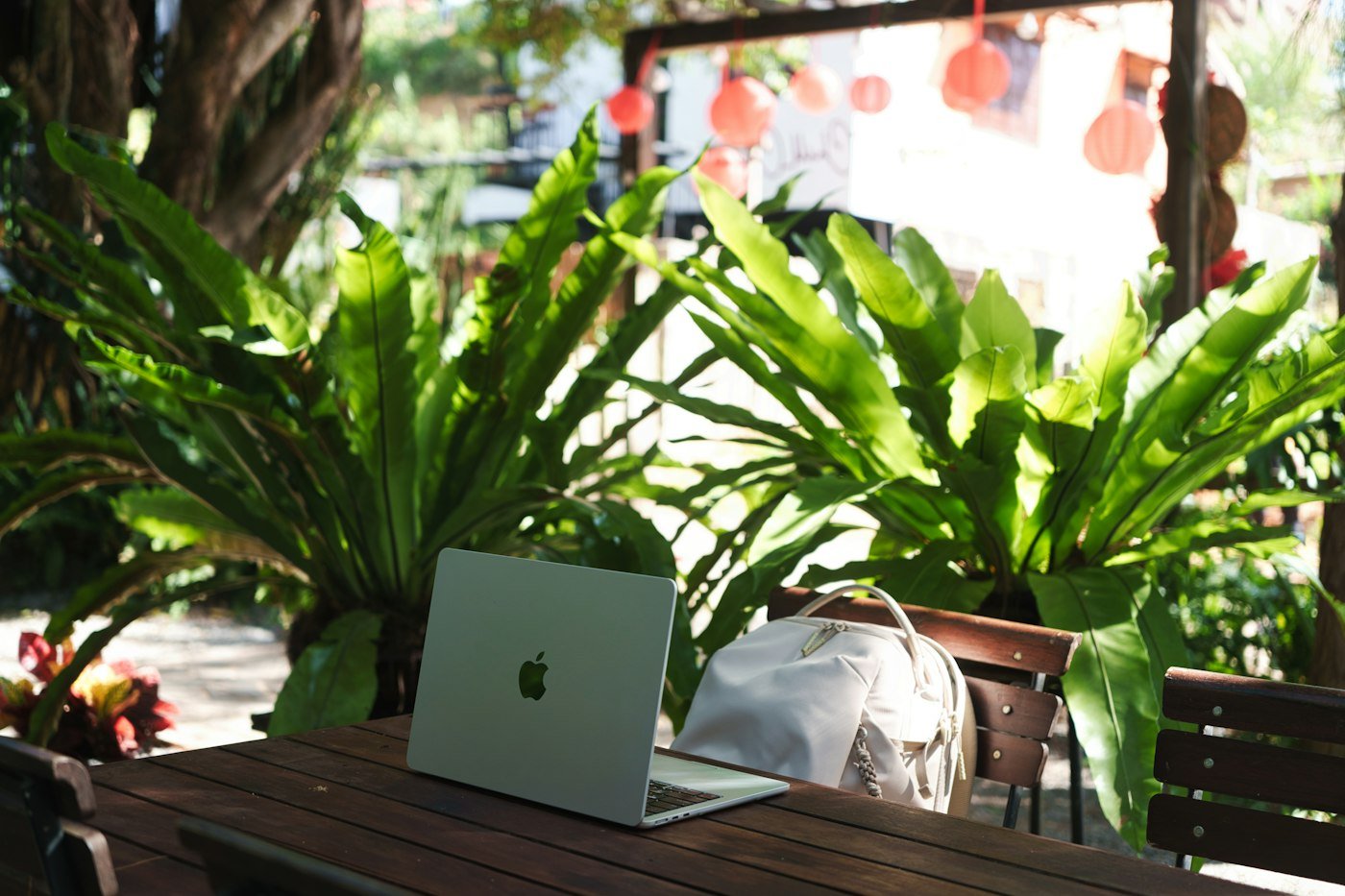 Laptop and backpack on a wooden table surrounded by tropical plants
